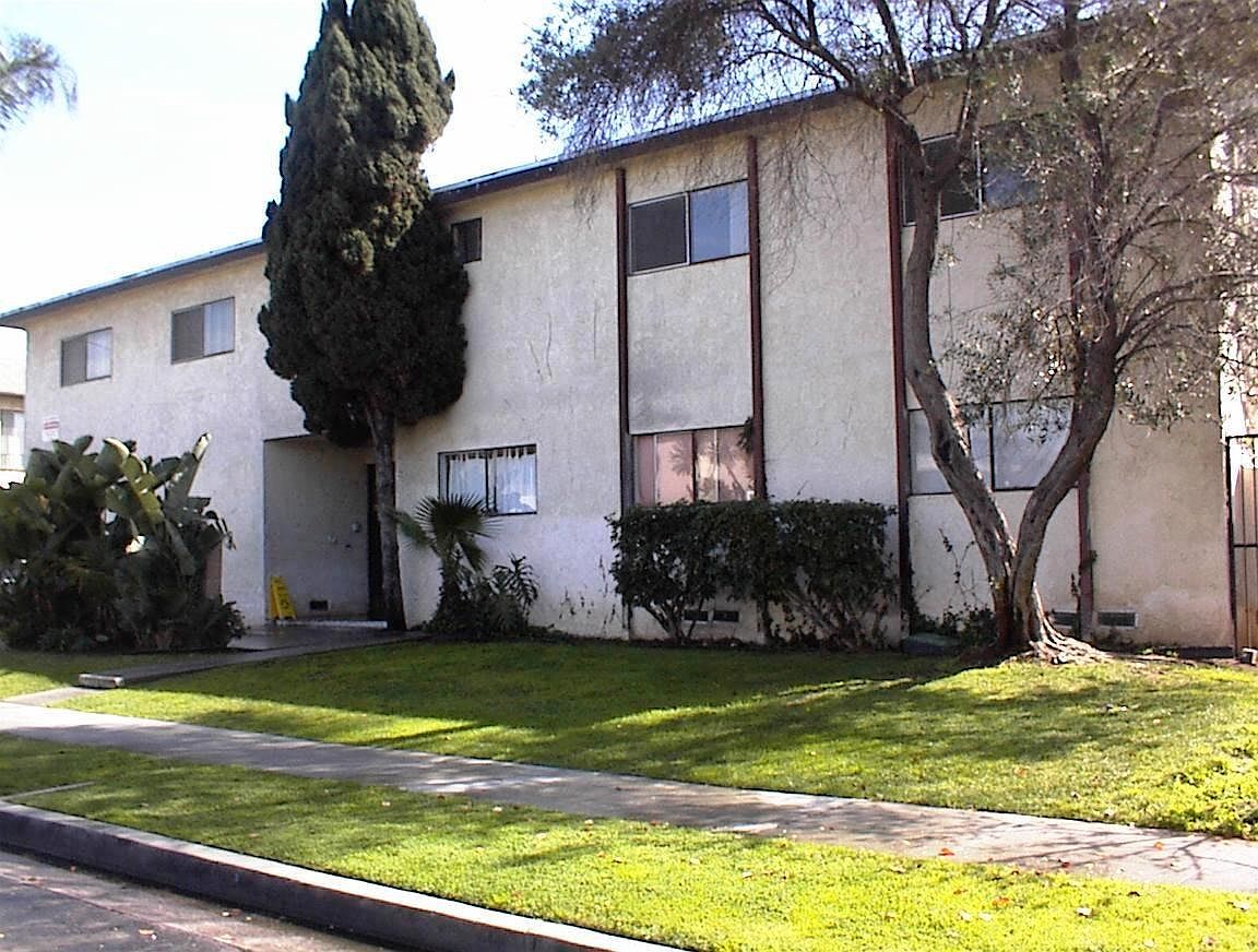 Two-story stucco apartment complex with tropical landscaping and exterior stairs